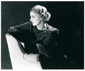 Lee Miller: "Autorretrato. Nueva York." (1932) - la imagen muestra a lee sentada en un sillón blanco. Se la ve en plano medio (de cintura para arriba) sobre un fondo negro. Lleva un vestido negro adornado con bordados también  negros, que sólo se aprecian en los hombros y el cuello. El rostro, de perfil mirando hacia la izquierda, está muy iluminado y la luz se refleja también en sus cabellos rubios recogidos en la nuca. Mira hacia abajo y tiene cierto aire de tristeza. Pulse para ampliar.