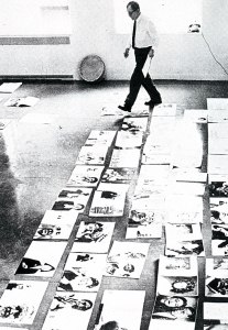 La imagen muestra una sala vista desde arriba. Sobre el suelo, desplegadas un montón de páginas dobles de revistas. Al fondo, de pie, paseándose entre ellas con un papel en la mano, Alexei Brodovitch.